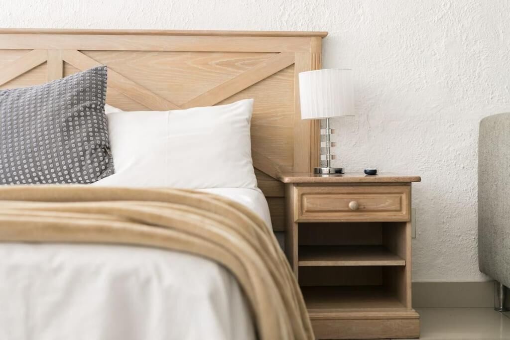 A neatly made bed with a wooden headboard, a bedside lamp, and a small wooden nightstand with a drawer.