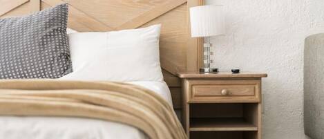 A neatly made bed with a wooden headboard, a bedside lamp, and a small wooden nightstand with a drawer.