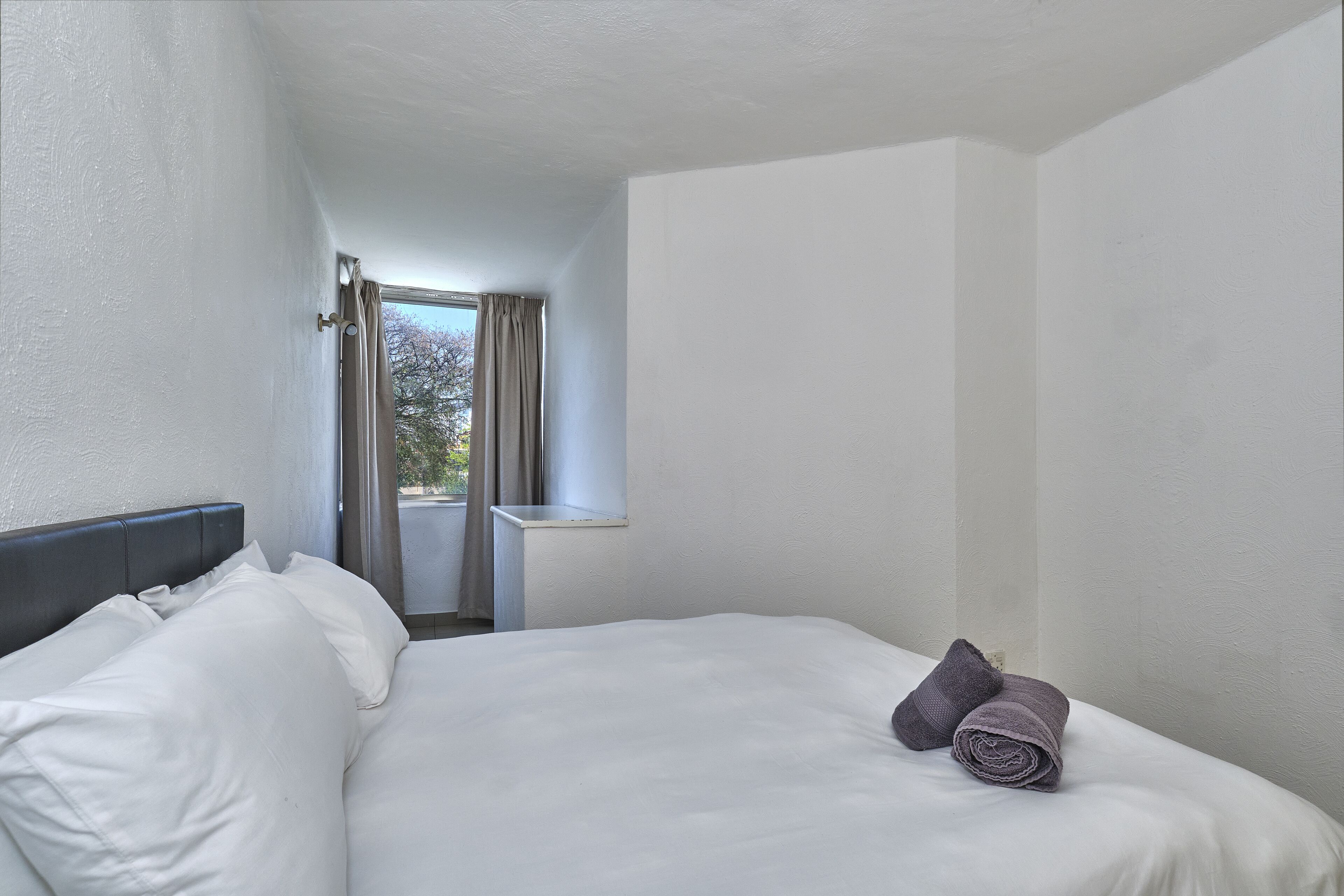 Habitación de hotel con cama, ventana con cortinas y vista a árboles.