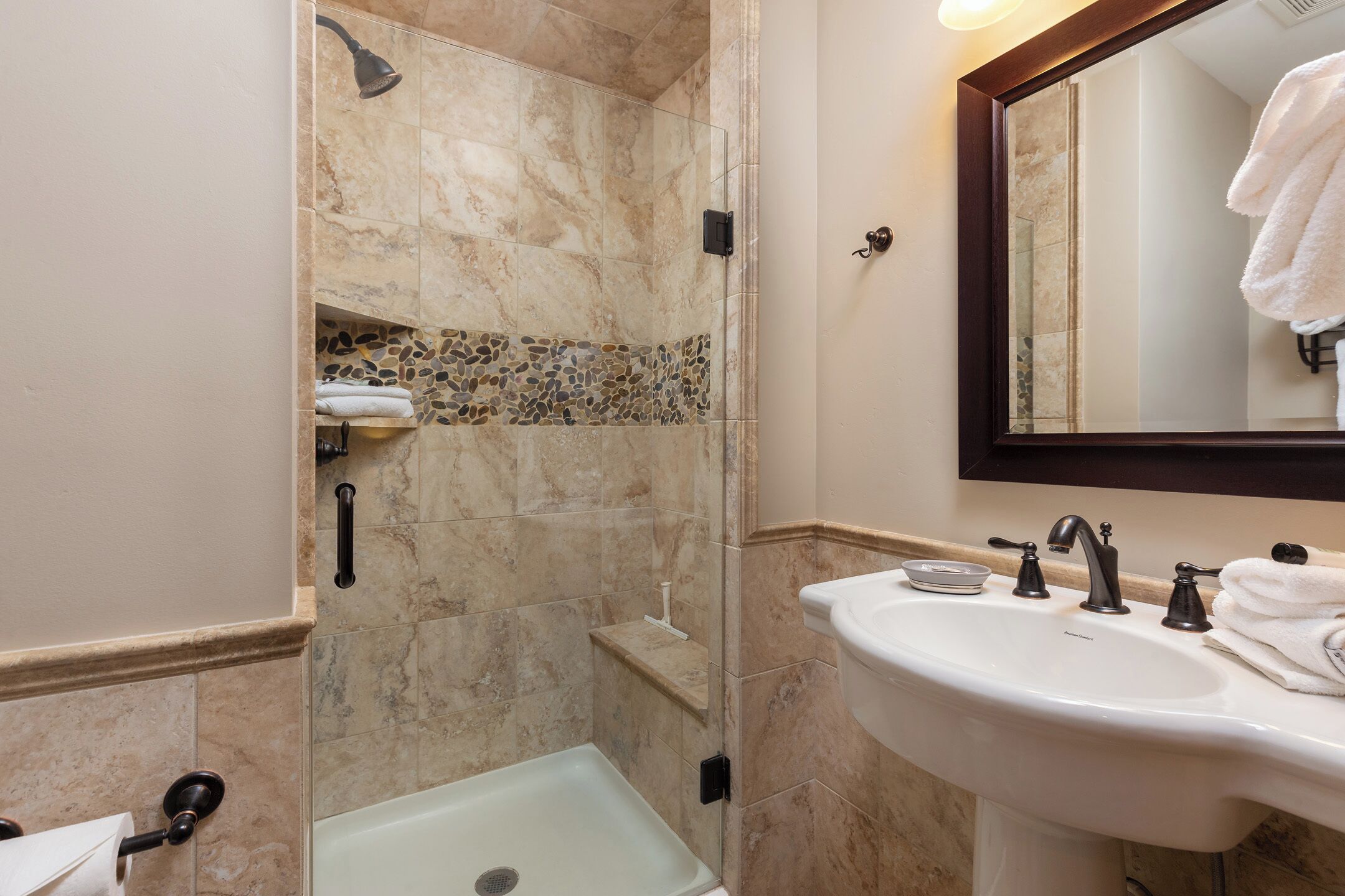 A bathroom with a glass-enclosed shower, a white sink with a mirror above it, and a towel rack.