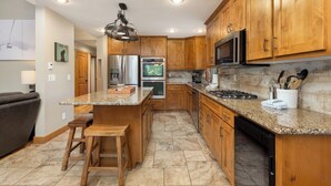 Una cucina moderna con mobili in legno, piani in granito, elettrodomestici in acciaio inossidabile e un'isola centrale con sgabelli.