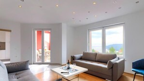 A modern living room with a grey sofa, a coffee table, and a large window offering a view of the outdoors. - Apartment Flores by Interhome (Rabac)