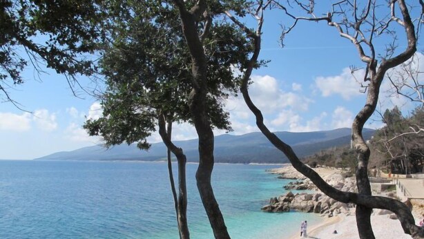 A coastal landscape with clear blue waters, rocky shoreline, and a few people on the beach. - Apartment Flores by Interhome (Rabac)