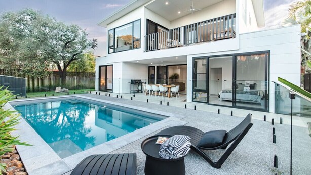 Ein modernes, zweistöckiges Haus mit Pool, Sitzgelegenheit im Freien und einem Balkon.