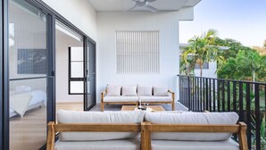 Ein Balkon mit einer Couch, einem Tisch, einem Deckenventilator und Blick auf Grünflächen.