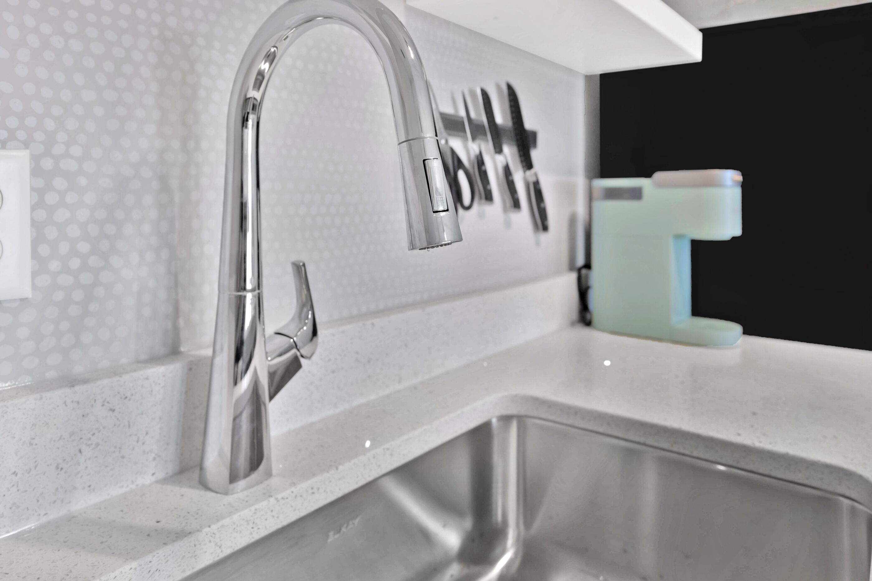 A modern kitchen with a stainless steel sink, a white countertop, and a wall-mounted faucet.