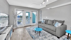 Een moderne woonkamer met een grijze bank, een blauwe salontafel en een televisie op een witte dressoir.