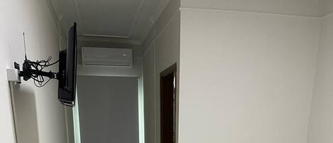 A small, clean room with a bed, a small table, a TV mounted on the wall, and a radiator.
