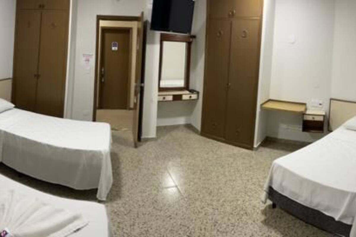 A hotel room with two single beds, a desk, a chair, a small table, a mirror, and a wardrobe.
