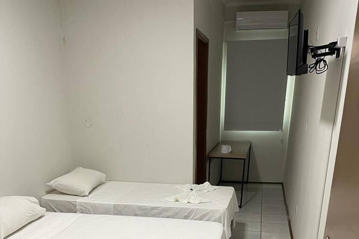 A small, clean room with two beds, a table, and a TV mounted on the wall.