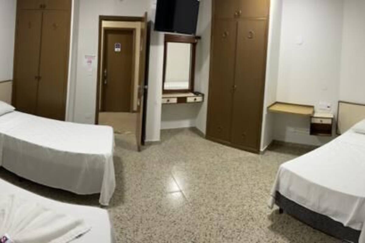 A hotel room with two single beds, a desk, a chair, a wardrobe, and a bathroom.