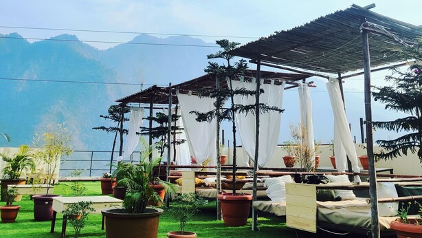 A rooftop terrace with multiple beds, potted plants, and a view of mountains. - Hotel Aqua Vibes (Rishikesh)