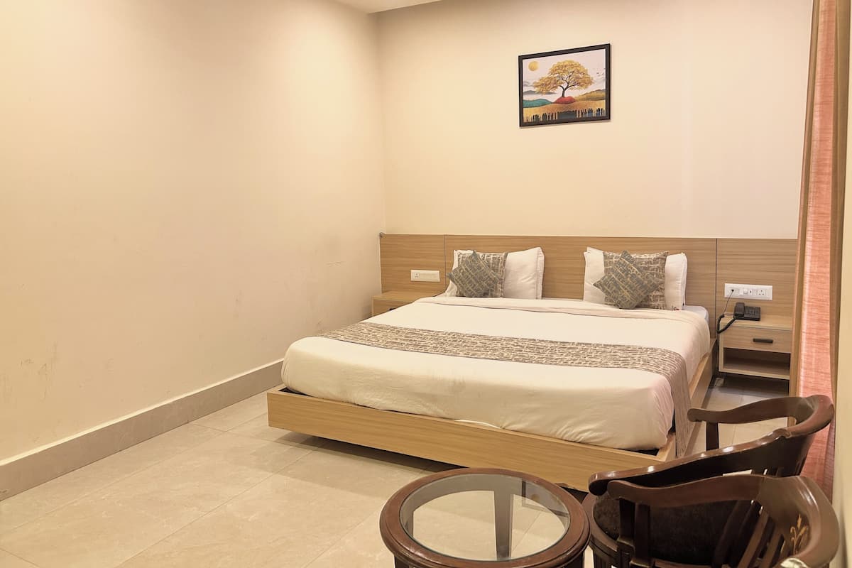 Una habitación de hotel con cama, mesita de noche, silla y un cuadro en la pared.