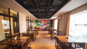 A restaurant with wooden tables and chairs, a colorful mural on the wall, and large windows allowing natural light. - Hotel Aqua Vibes (Rishikesh)