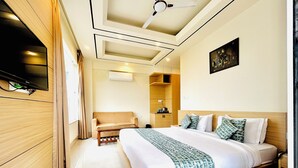 A modern hotel room with a large bed, a sofa, a TV, and a ceiling fan. - Hotel Aqua Vibes (Rishikesh)