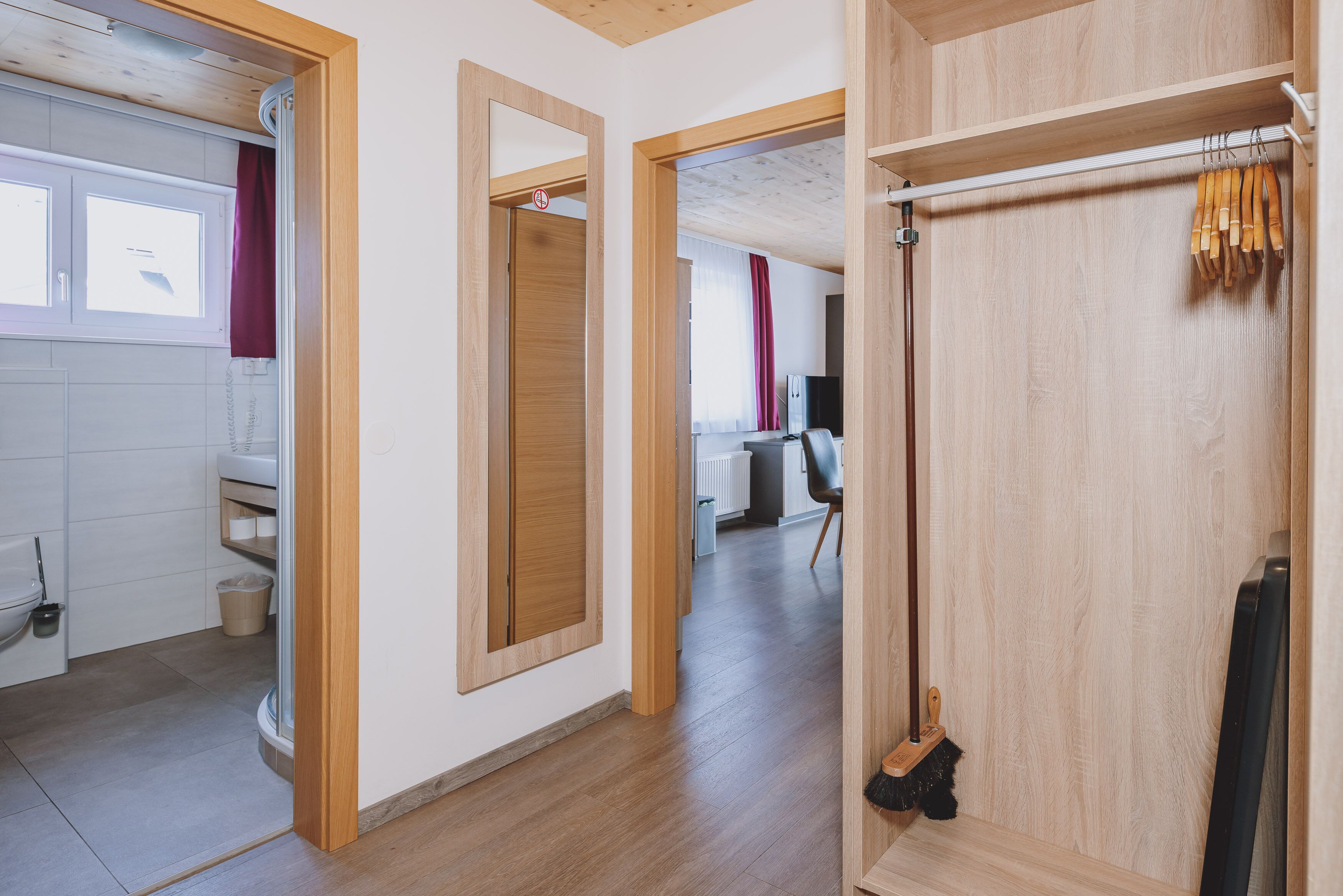 A modern interior with wooden flooring, a visible bathroom with a toilet, and a hallway leading to a room with a radiator and a chair.