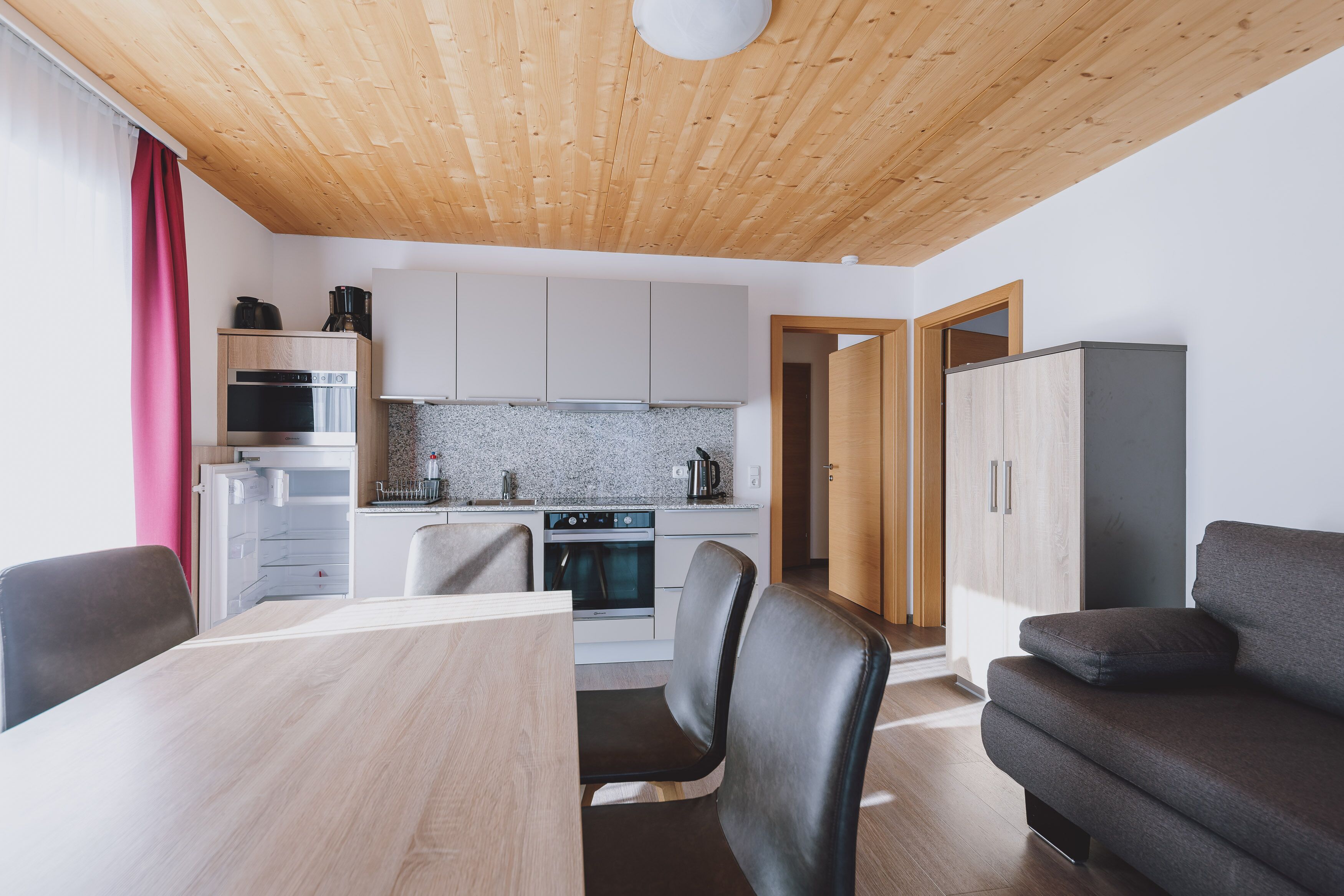 Una cucina moderna con mobili bianchi, forno integrato e microonde. C'è un tavolo da pranzo con sedie e un divano nella zona living.