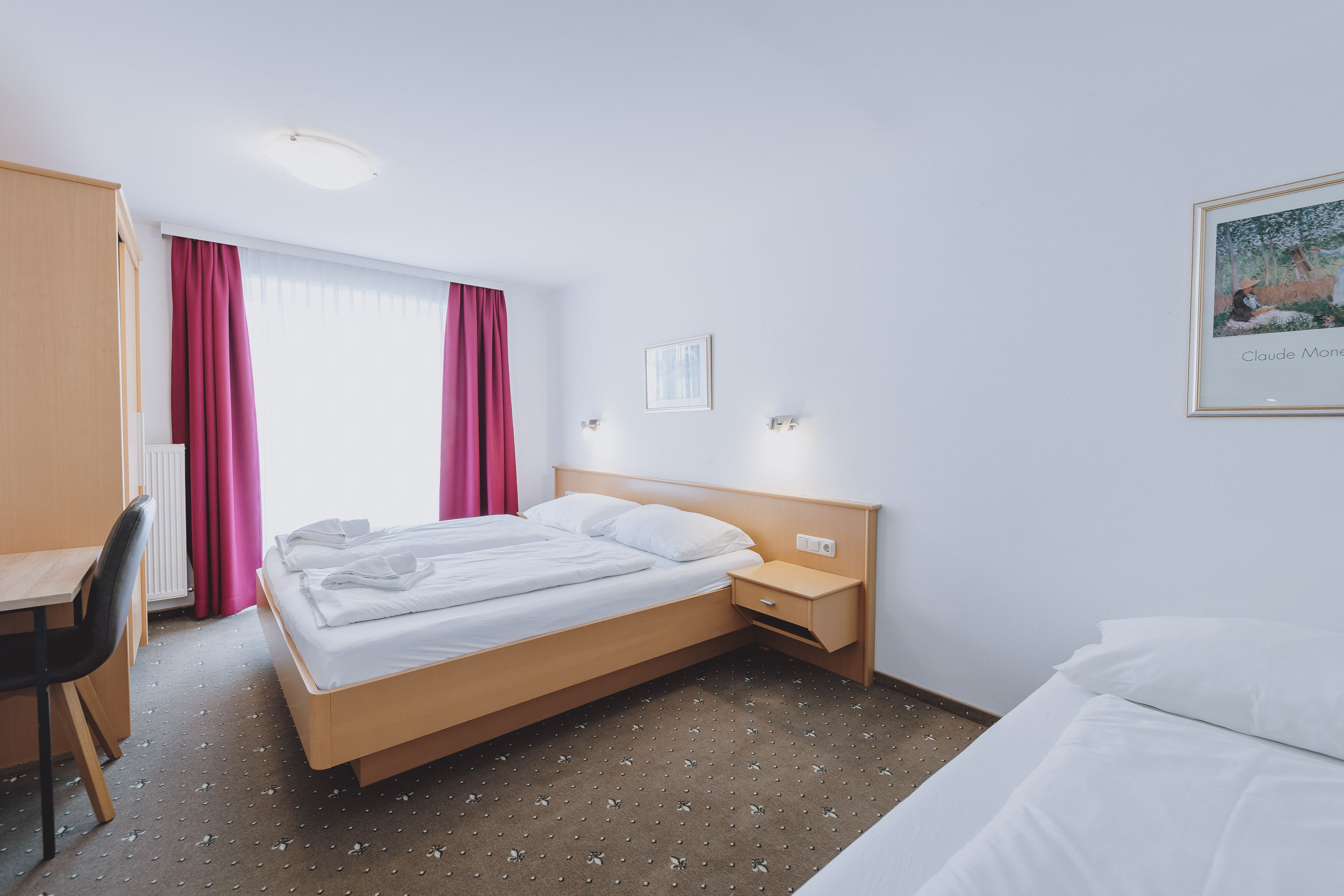 A hotel room with a bed, bedside table, and a desk with a chair.