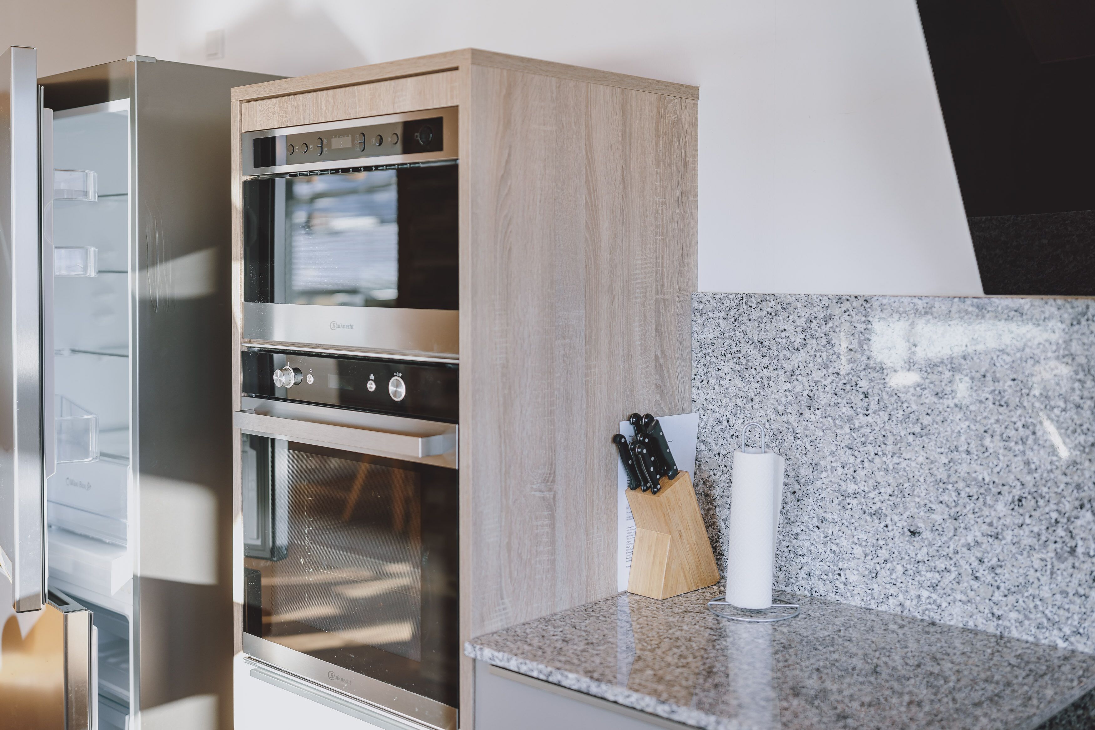 A modern kitchen with a built-in oven, a granite countertop, and a knife block.