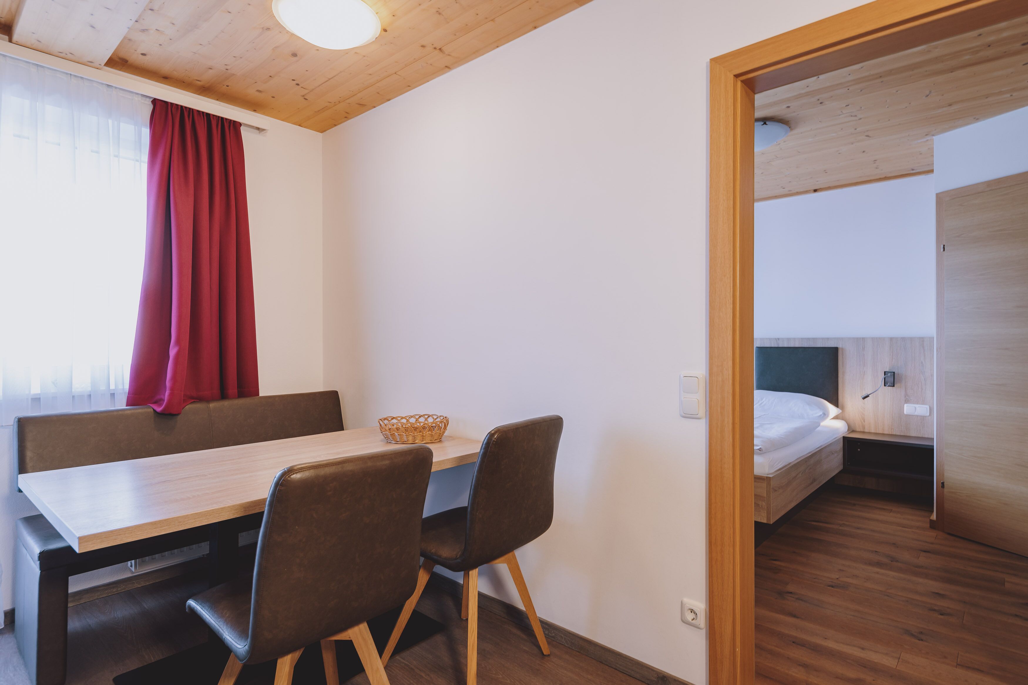 A compact room with a wooden table, two chairs, a small bench, a bed, and a wooden floor.