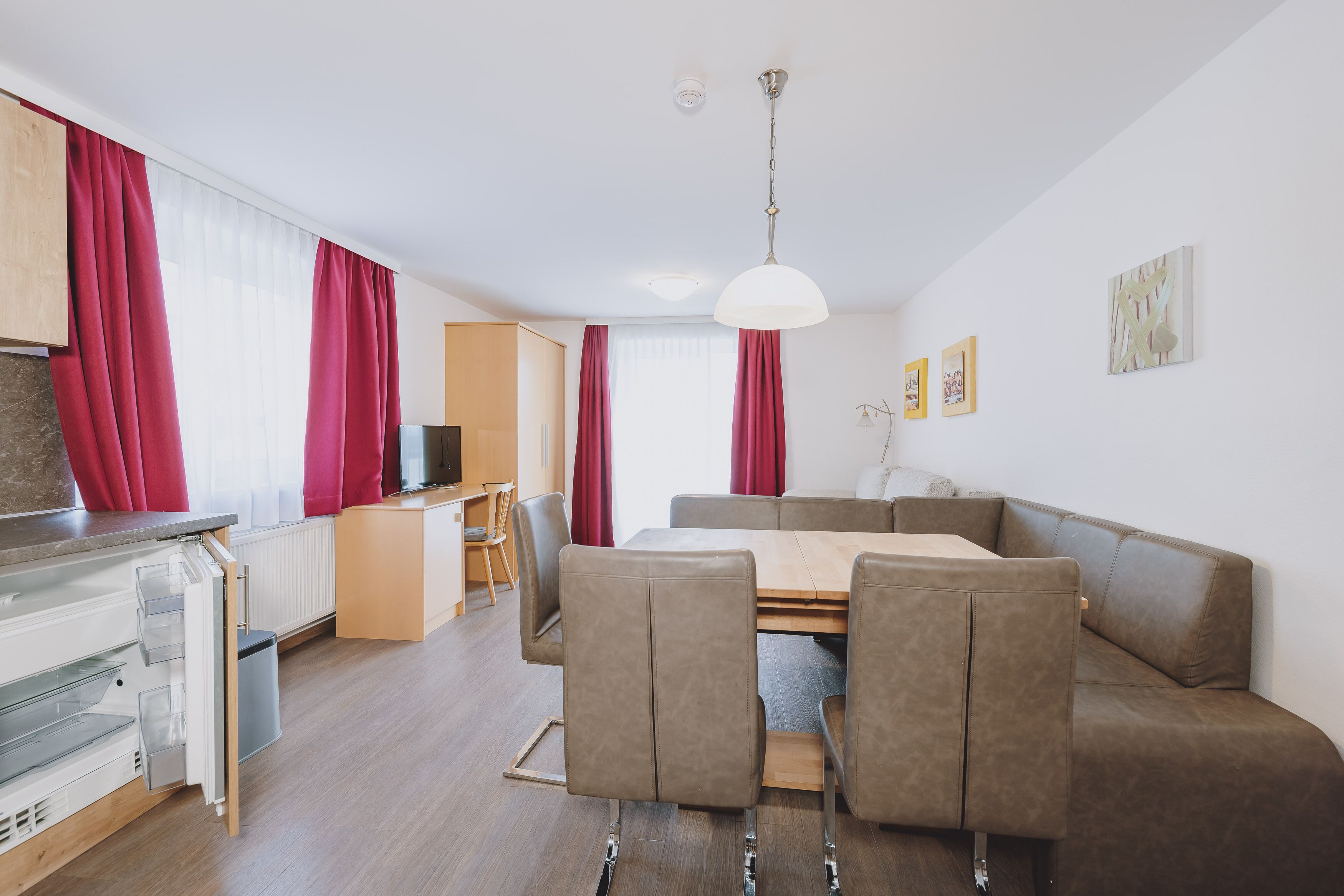 A modern living room with a dining table, sofa, and chairs. There is a kitchen area with a refrigerator and a microwave.