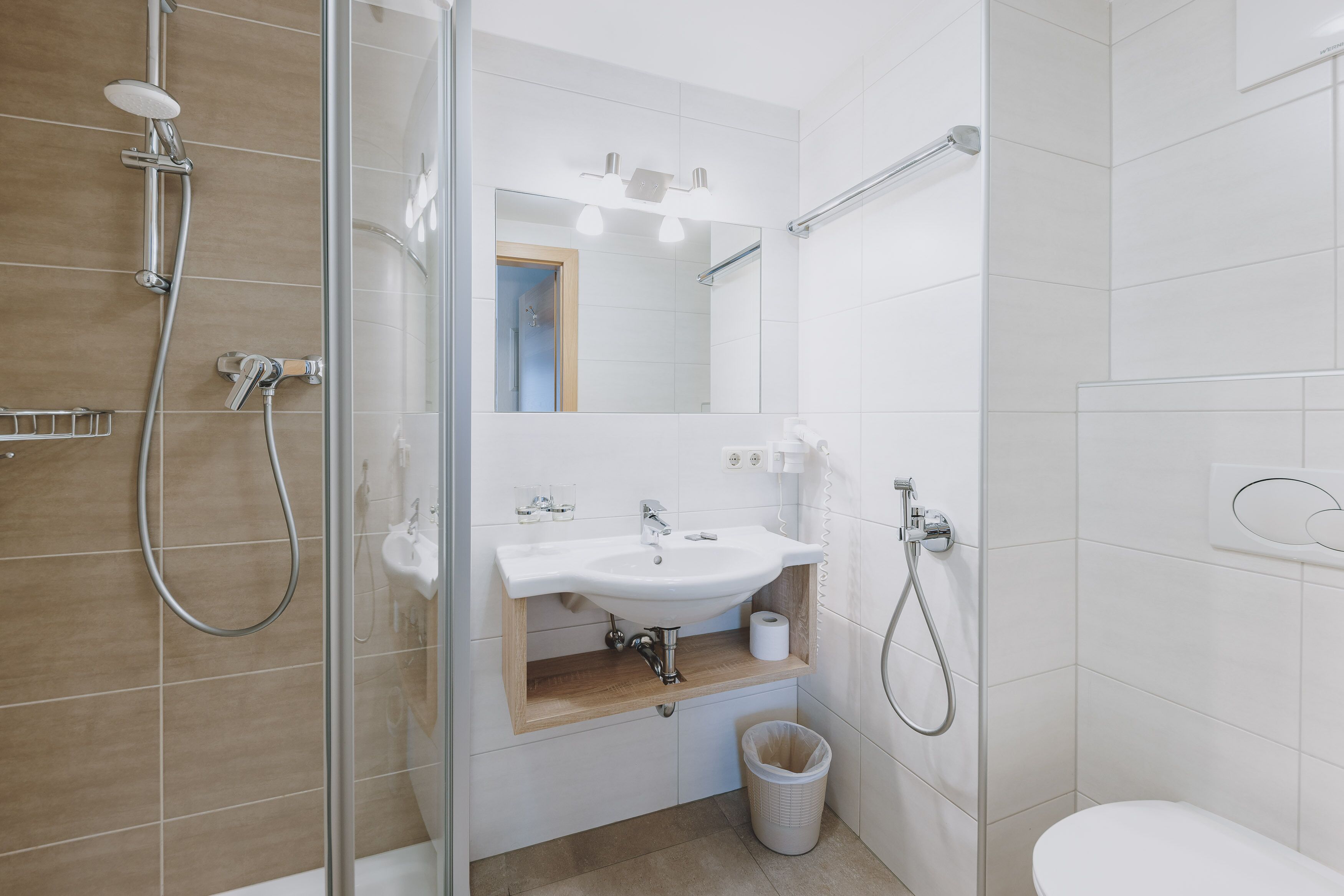 A modern bathroom with a glass shower enclosure, a white sink with a wooden countertop, and a white toilet.