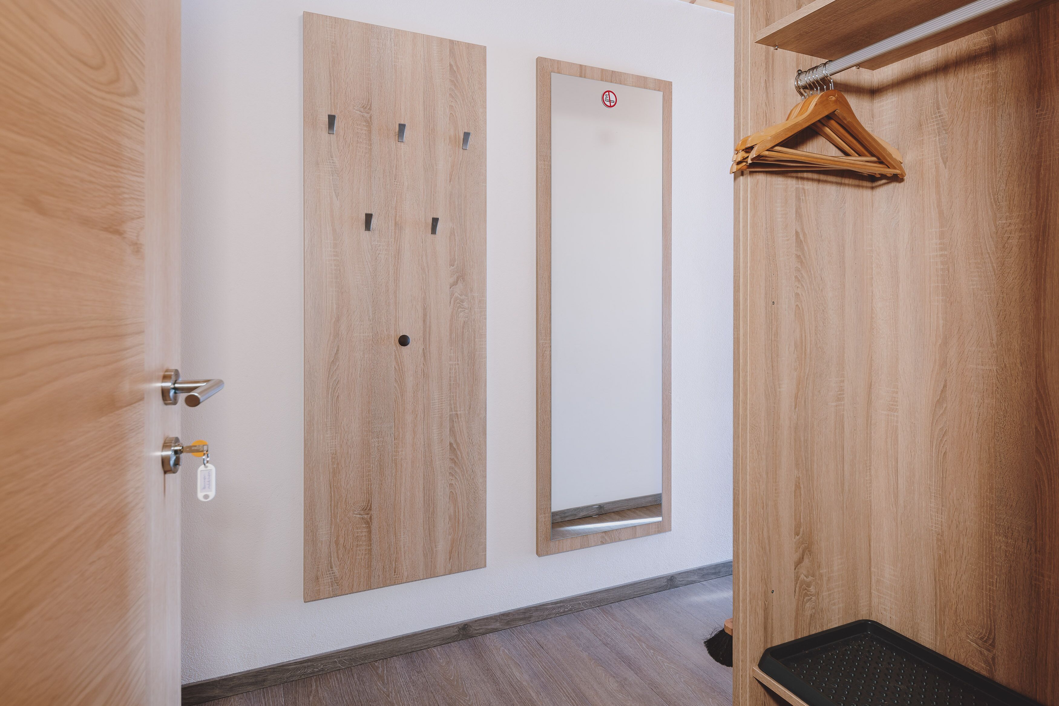 A wooden door with a handle and a key lock, a mirror, and a wooden hanger on the wall.
