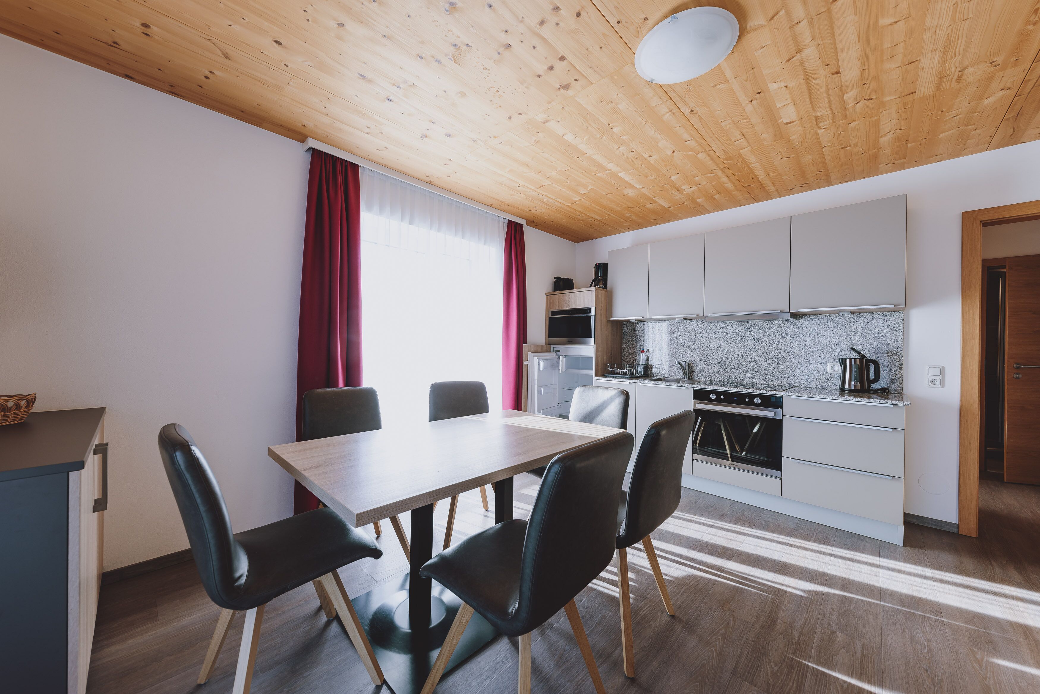 A modern kitchen with white cabinets, a wooden ceiling, and a dining area with a table and chairs.