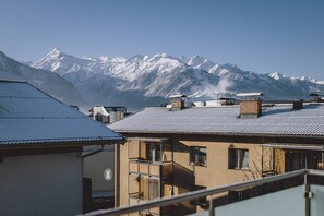 Edifici residencial amb teulada metàl·lica, un balcó i vista a les muntanyes nevades.