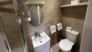 A modern bathroom with a glass shower enclosure, a white sink, a round mirror, and a toilet. - Parkhouse Bed and Breakfast (Bunratty)