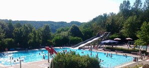 Une piscine avec un toboggan, entourée d’arbres et située dans un paysage vallonné.