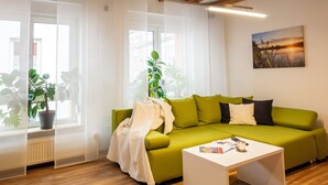 Una sala de estar con un sofá verde, una mesa de centro blanca y un ventanal con cortinas de gasa.