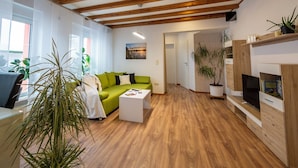 Una sala moderna con un sofá verde, una mesita de centro blanca, suelo de madera y un televisor sobre un mueble de madera.