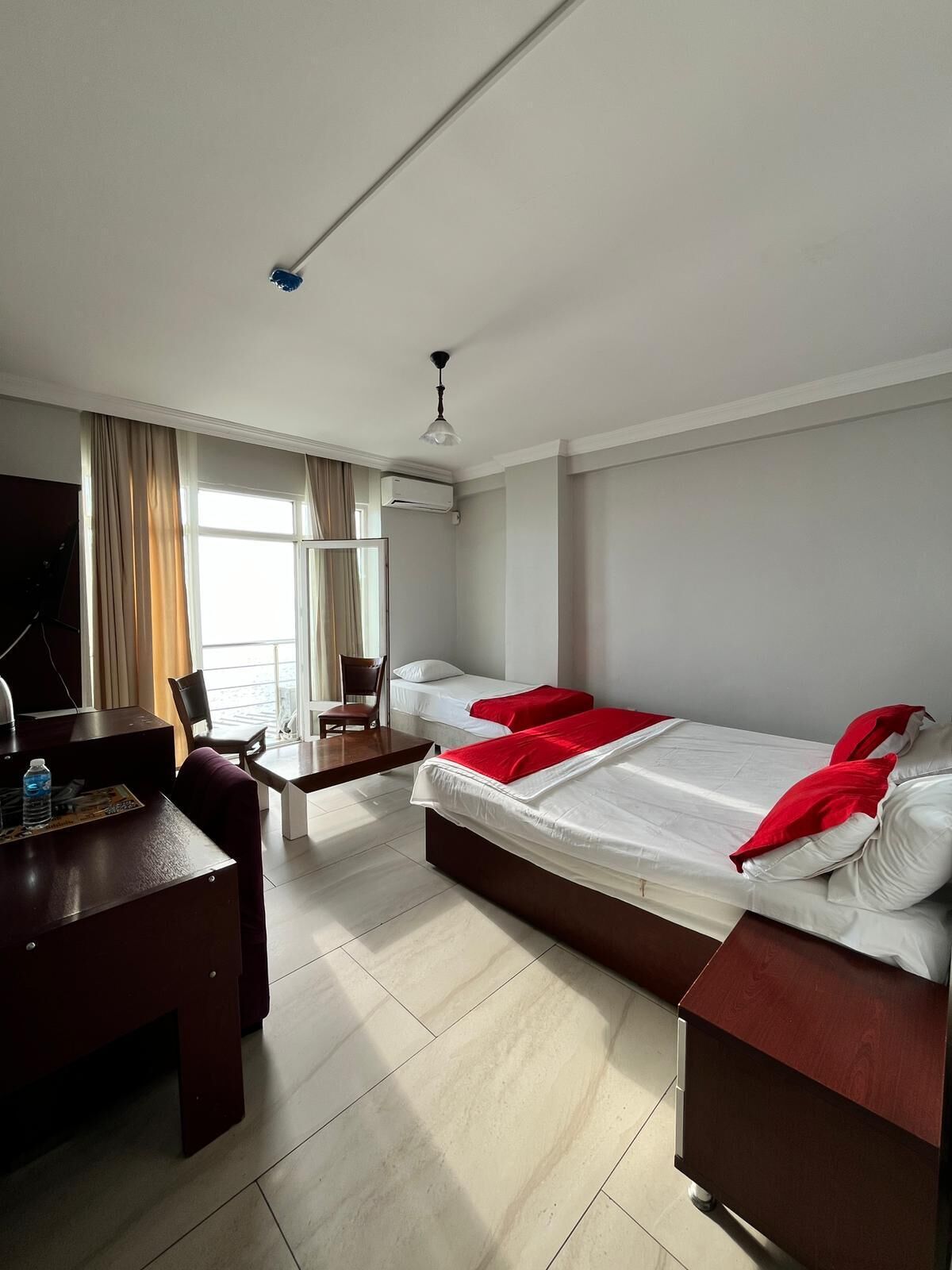 A hotel room with a desk, two beds, a chair, a TV, and an air conditioning unit.