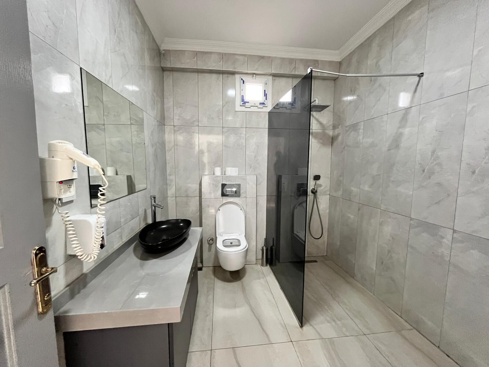 A modern bathroom with a toilet, bidet, and a glass shower enclosure.