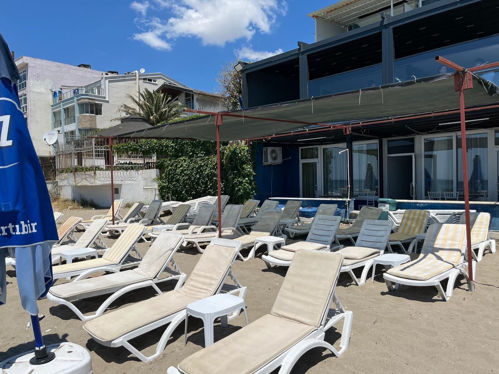 Une zone aménagée au bord de la plage, avec des chaises longues, des parasols et un bâtiment doté de grandes fenêtres.