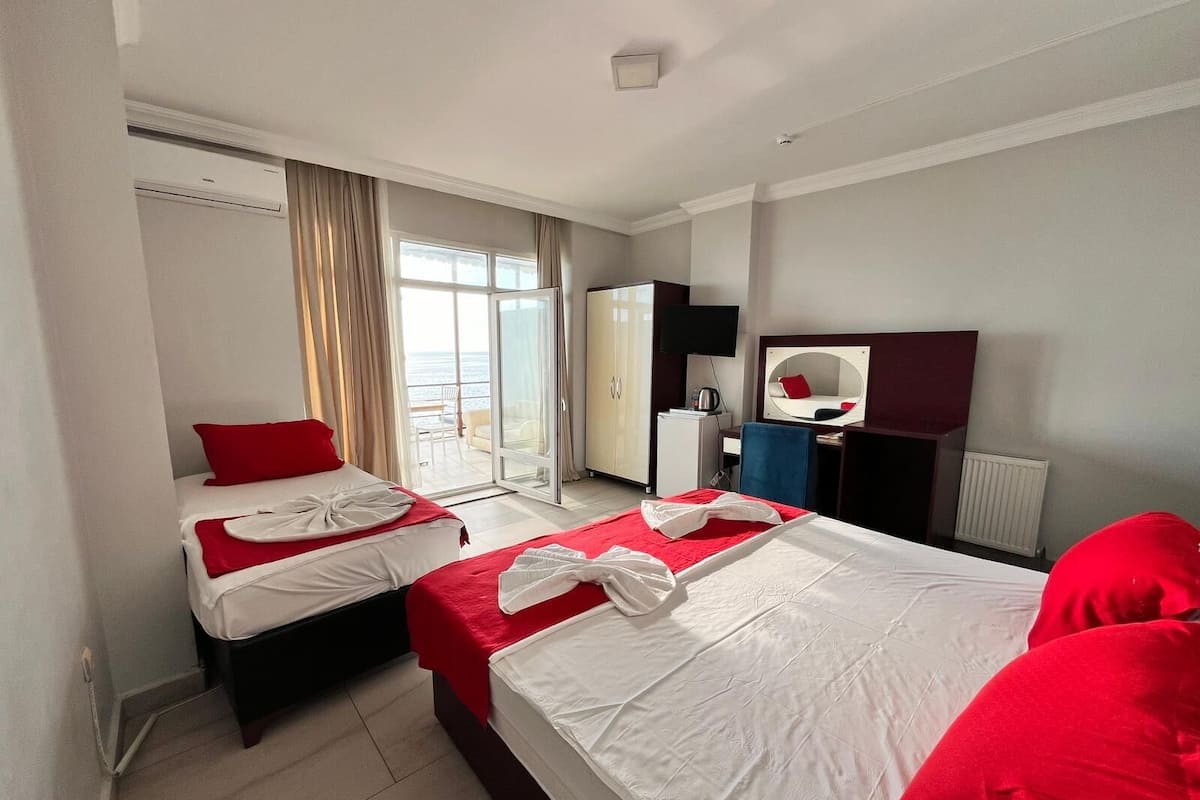Habitación de hotel con dos camas, televisión, escritorio, espejo y vista al mar.