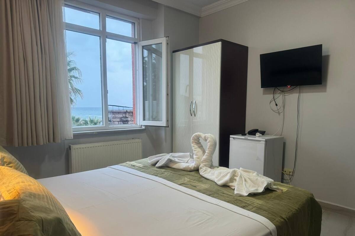 Habitación de hotel con cama, armario, escritorio, televisor y ventana con vista al mar.
