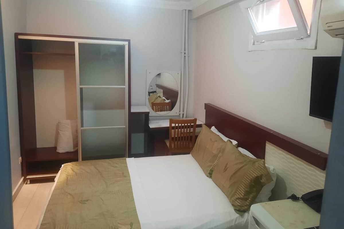 Una habitación de hotel con cama, escritorio, silla, armario, espejo y televisión.