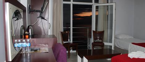 Habitación de hotel con escritorio, sillas, cama y ventana grande con vistas.