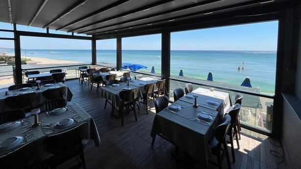 Un área de comedor al aire libre con mesas preparadas para dos, con vista a una playa y al mar.