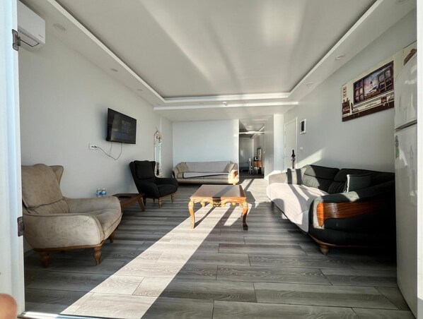 A modern living room with a sofa, armchair, coffee table, and a flat-screen TV mounted on the wall.