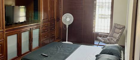 Une chambre à coucher avec un lit, une armoire en bois, un ventilateur de plafond et une chaise.