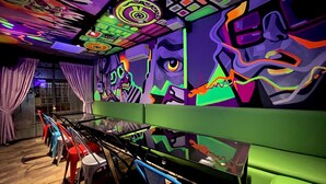 A room with vibrant graffiti art on the walls, a green sofa, and a glass table. - Ámbar Hostel  San Gil (San Gil)
