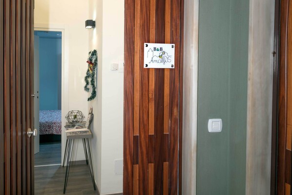 Un pasillo con una puerta de madera, una puerta azul al fondo, y una pequeña mesa con una planta y un marco de fotos.