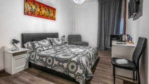 Un dormitorio moderno con una cama grande, un escritorio, una silla, una mesita de noche, un cuadro y una araña.