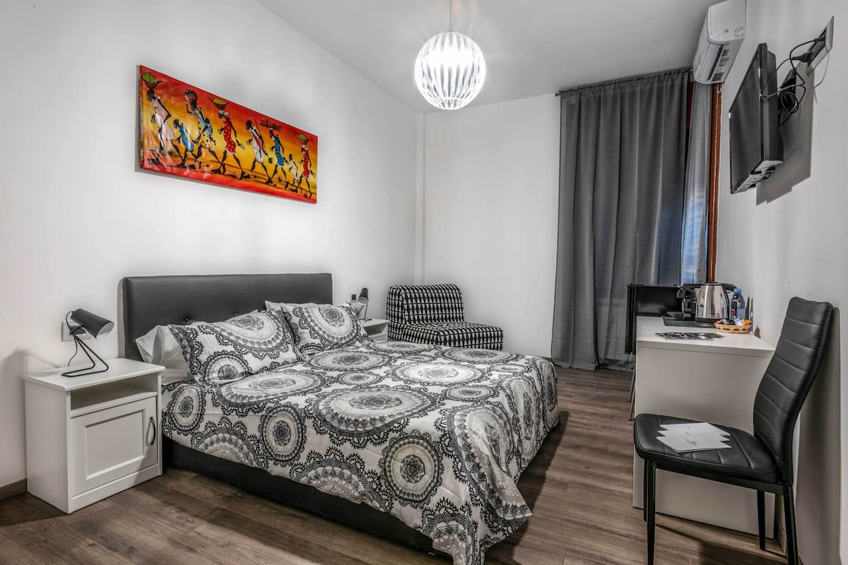 Un dormitorio moderno con una cama grande, un escritorio, una silla, una mesita de noche, un cuadro y una araña.