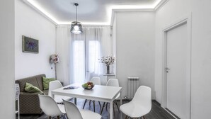 Un comedor moderno con una mesa y sillas blancas, un sofá estampado y un jarrón decorativo.