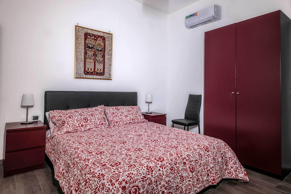 Un dormitorio con cama, mesita de noche, silla, armario y aire acondicionado instalado en la pared.