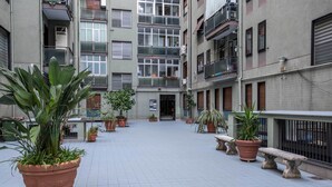 Un patio con plantas en macetas, un banco y la entrada de un edificio.